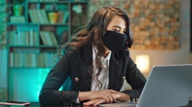 Ofisteki güzel kadın, kameranın önünde dizüstü bilgisayardan koruyucu maske takarak Coronavirus 2019 'da internetten toplantı yapıyor.