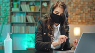 Ofisteki karantinada bir bayan ofis çalışanı dizüstü bilgisayardaki işine başlamadan önce ellerini jöle ile dezenfekte etti sonra da çalışmaya devam etti koruyucu bir maske takarak Coronavirus 2019