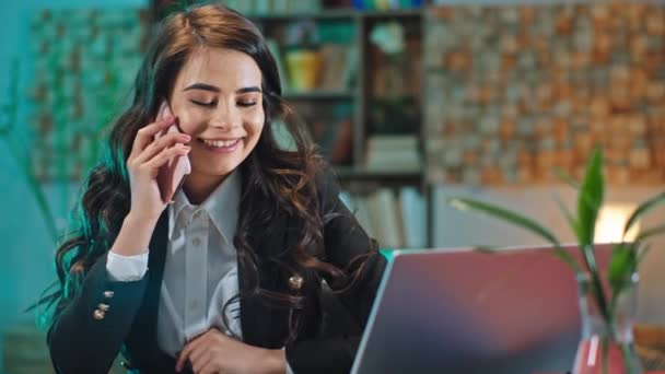 Grande employée de bureau souriante dans le bureau elle a une conversation excitée au téléphone alors qu'elle est assise à son lieu de travail — Video