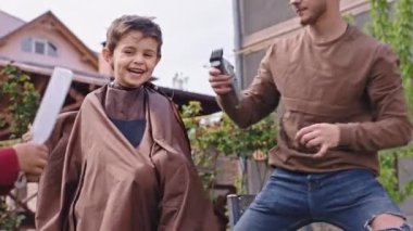 Gülümseyen şirin çocuk, bahçede oturmuş eğleniyor. Saçını kesmeye hazırlanıyor. Saçını kesmeye başlıyor. ARRI Alexa Mini 'de çekilen