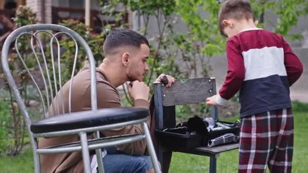 Buen momento hermano mayor pasar con su hermano pequeño lindo que explicar y mostrar las herramientas de corte de pelo que pasan un buen rato juntos — Vídeo de stock