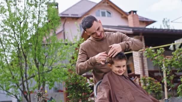 Sonríe chico lindo grande tener un corte de pelo en el jardín fuera del barbero hermano mayor hacer el corte de pelo — Vídeos de Stock