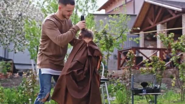 En el jardín en casa hermano mayor hacer un corte de pelo de su hermano pequeño rápidamente con un cortador electrónico — Vídeo de stock
