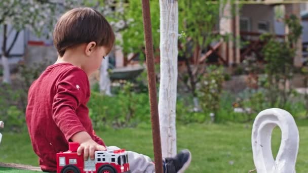 Di kebun hari yang cerah tiga saudara bersenang-senang bermain bersama di rumput yang terkecil makan permen lolipop — Stok Video
