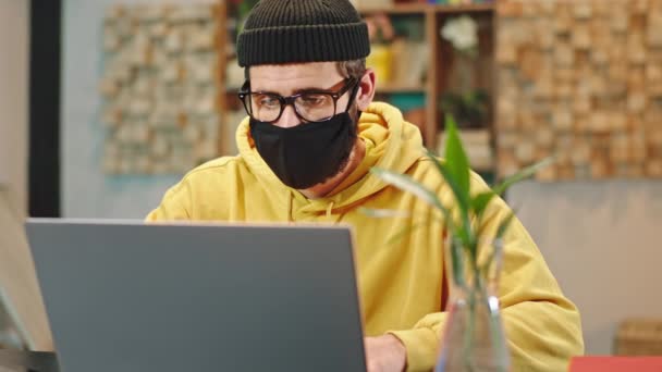 Em casa na frente da câmera carismático cara concentrado com uma máscara protetora fazendo seu curso on-line formar a faculdade que ele está estudando formar o laptop — Vídeo de Stock