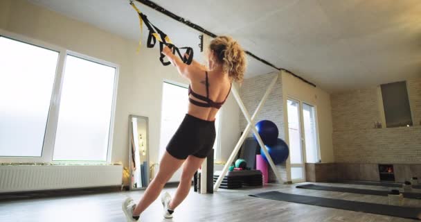 В просторной студии аэробная леди практикует новый TRX упражнения спортивной деятельности для молодой женщины с светлыми волосами в спортивной одежде — стоковое видео