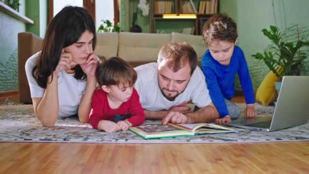 Genç anne ve baba evde iki çocuğuyla vakit geçiriyorlar kitap okuyorlar ve birlikte iyi vakit geçiriyorlar. — Stok video