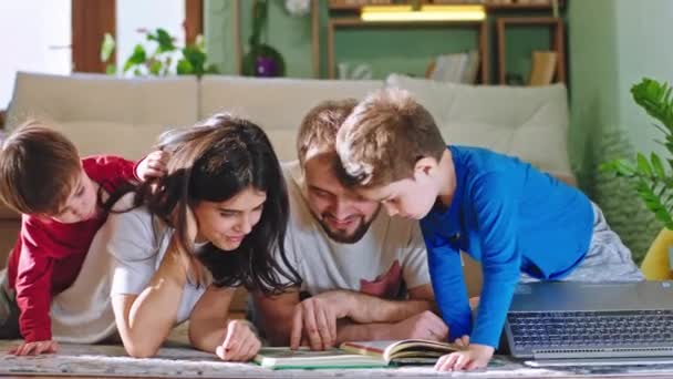 Parents heureux passer du bon temps ensemble tout en s'asseyant sur le sol ils lisent un livre d'histoire souriant grand profiter du temps — Video