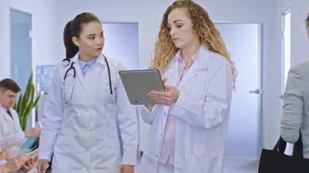Před kamerou na moderní nemocnici na chodbě dvě lékařky analyzují a diskutují diagnostiku pacienta a léčbu pomocí digitálního tabletu na pozadí — Stock video