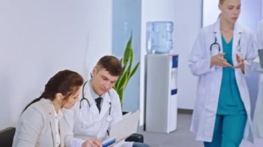 Modern hastane koridorunda doktorlar hastayla kameranın karşısına geçip hastanın teşhisini tartışan diğer iki genç doktorla görüşüyor.