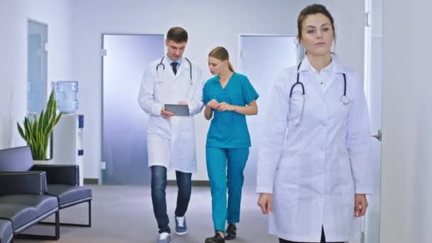 Dojrzała kobieta lekarz idący korytarzem szpitala na tle innego lekarza mężczyzna i jego pielęgniarka pani omawiając przyszłe leczenie dla pacjenta — Wideo stockowe