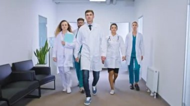 Modern özel hastanede koridordaki büyük doktorlar ve hemşireler kameranın önünde durup kameraya bakıyor.