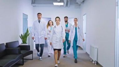 Genç ve olgun doktor ve hemşirelerden oluşan bir ekip hastane koridorunda kameranın önüne geçip tıp ve sağlık hizmetleri konseptine bakıyorlar.