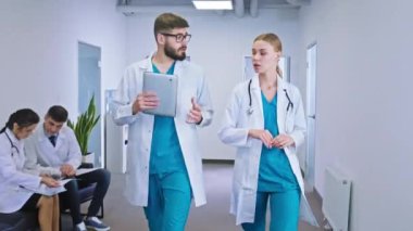 İyi görünümlü bayan doktor ve erkek hemşire hastane koridorunda hasta geçmişinin analizini yapıyorlar. Sandalyede oturan diğer doktor.