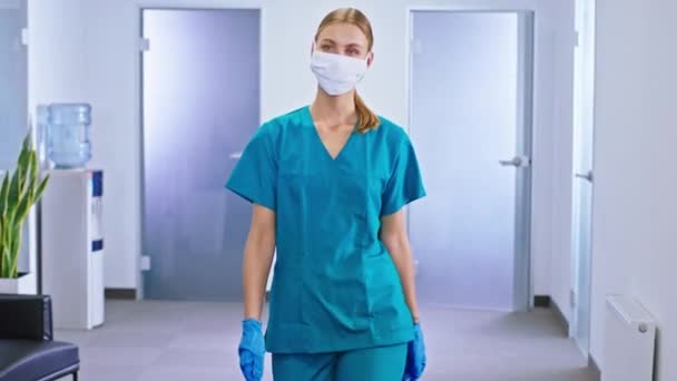 Carismatica infermiera donna dopo l'intervento chirurgico cammina in ospedale corridoio con una maschera protettiva davanti alla telecamera — Video Stock
