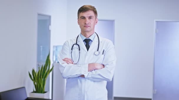 Retrato de un hombre los médicos con una cara seria delante de la cámara mirando recto tienen un estetoscopio en el cuello que se para en el pasillo del hospital — Vídeos de Stock