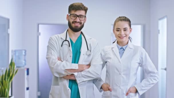Auf dem Krankenhausflur posieren ein Arzt und eine Krankenschwester charismatisch und gut aussehend mit einem breiten Lächeln vor der Kamera — Stockvideo