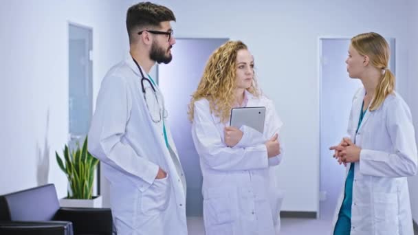 Twee artsen en een verpleegkundige hebben een discussie in de hoofdgang van het ziekenhuis ze analyseren van de toekomstige behandeling voor de patiënt — Stockvideo