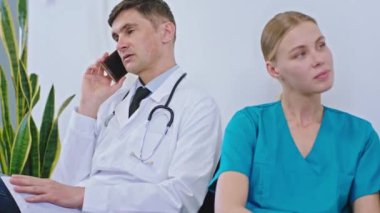 Kameranın önünde olgun bir doktor diğer doktor ve hemşireyle birlikte hastanede oturuyor. Ara veriyorlar. Telefonda konuşuyor. İki bayan sosyalleşiyor.