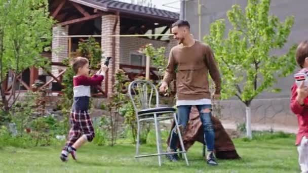 Na trawie w domu dwoje charyzmatycznych małych dzieci bawiących się ze swoim starszym bratem spędzają razem miło czas — Wideo stockowe