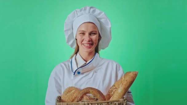 Dentro de un estudio de croma key atractiva señora panadero con una gran sonrisa grande sosteniendo una cesta de un pan francés fresco delante de la cámara. Disparo en ARRI Alexa Mini — Vídeo de stock