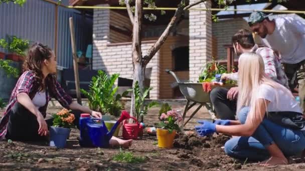 Grupo de amigos en el jardín se divierten sentados en el suelo y se preparan para comenzar a plantar las plantas y flores disfrutando del tiempo en la naturaleza. Disparo en ARRI Alexa Mini — Vídeos de Stock