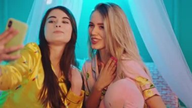 Mutlu ve karizmatik öğrenciler kampüs yatak odasında pijamalarıyla oturmuş akıllı telefon kullanarak fotoğraf çekiyor ve büyük bir gülümseme sergiliyorlar. ARRI Alexa Mini 'de çekilen