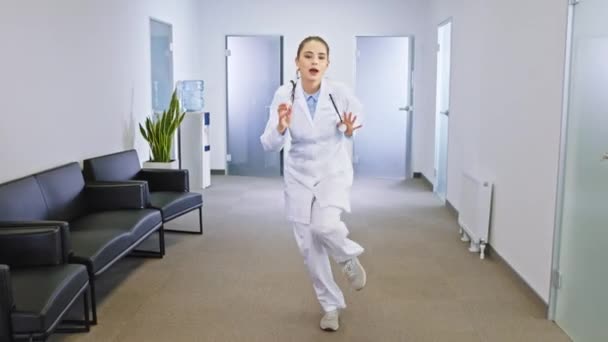 Улыбающаяся большая молодая доктор танцует взволнованная перед камерой и наслаждается временем на своем рабочем месте. Снимок на ARRI Alexa Mini — стоковое видео