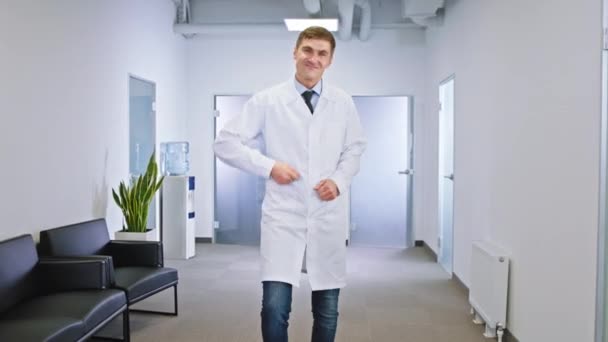 Bardzo atrakcyjny główny lekarz w środku nowoczesnego szpitalnego korytarza tańczący i uśmiechnięty duży — Wideo stockowe