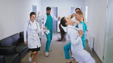 Modern bir hastane koridorunda dans ederken kameranın önünde büyük bir gülümsemeyle doktorlar ve hemşireler heyecanlanır.