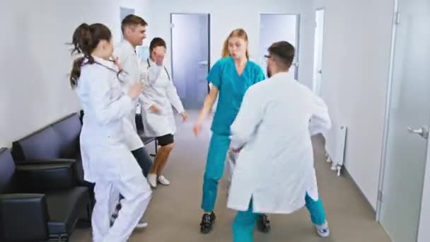 Skupina mladých a dospělých lékařů a sester tančících vzrušeně před kamerou v moderní nemocniční chodbě — Stock video