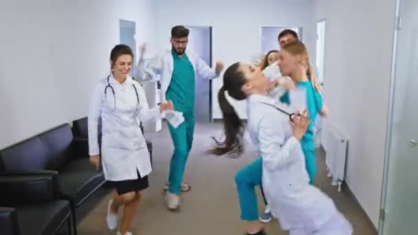 En un moderno pasillo del hospital bailando excitados médicos y enfermeras con una gran sonrisa delante de la cámara — Vídeos de Stock
