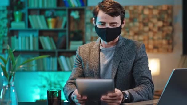 Coronavirus έννοια υπάλληλος γραφείου κάθεται στο χώρο εργασίας του και με μια προστατευτική μάσκα εργασίας στο φορητό υπολογιστή του πολύ συμπυκνωμένο — Αρχείο Βίντεο