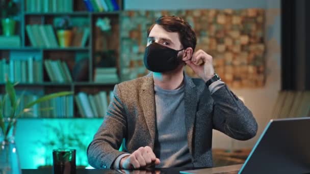 Retrato de un director ejecutivo en su lugar de trabajo que trabaja en el portátil con una máscara protectora y luego quitarse la máscara y hacer una cara feliz — Vídeos de Stock