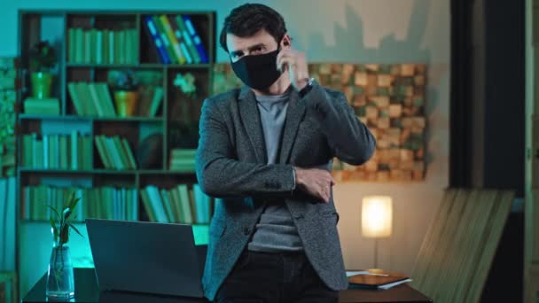 カメラをまっすぐに見る彼の職場で保護マスクを持つオフィスワーカーは、マスクを脱いでリラックスした笑顔の大きなコロナウイルス2019 — ストック動画