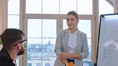 Büyük gülüşlü karizmatik bir iş kadını meslektaşlarıyla bir eğitim sunumu semineri düzenledi. Bazı liderlik fikirlerini açıkladı ve beyaz tahtadaki istatistikleri analiz etti.