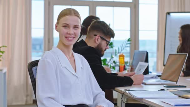 Muy hermosa señora en el retrato de la reunión mirando directamente a la cámara mientras que tienen una reunión de oficina en la mañana, entonces ella continuó haciendo algunas notas en su cuaderno — Vídeo de stock