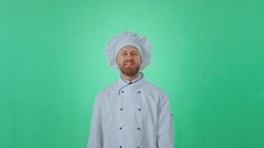 Kameranın önünde yeşil bir stüdyoda fırıncı kılığında üniformalı bir adam poz veriyor. Zamanın tadını çıkarıyor ve kameraya bakıyor.
