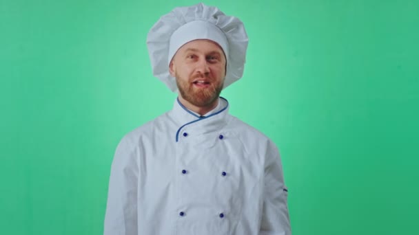 Зеленый фон стены очень харизматичный и взволнованный пекарь позирует перед камерой он показывает хорошо и мигает из одного глаза — стоковое видео