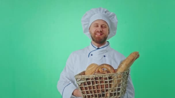 Grüner Hintergrund attraktiver Bäcker Mann mit einem Korb mit frischem Brot blickt direkt in die Kamera lächelt groß und zeigt den Korb Nahaufnahme in die Kamera — Stockvideo