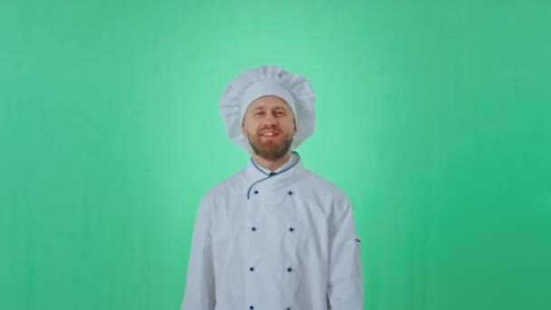 Delante de la cámara en un estudio verde posando hombre panadero sonriendo grande en un uniforme que disfruta del tiempo mirando directamente a la cámara — Vídeo de stock