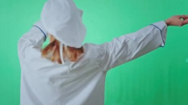 Mutlu ve karizmatik fırıncı kadın büyük yeşil bir arka plan stüdyosunda kameranın önünde dans ediyor ve gülümsüyor.