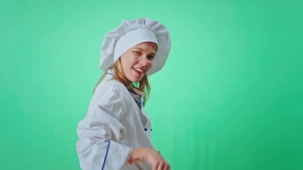 Baker woman in a uniform have a good time in a green studio playing with a fresh pretzel in front of the camera and smiling large looking straight make a pretty face — Stock Video