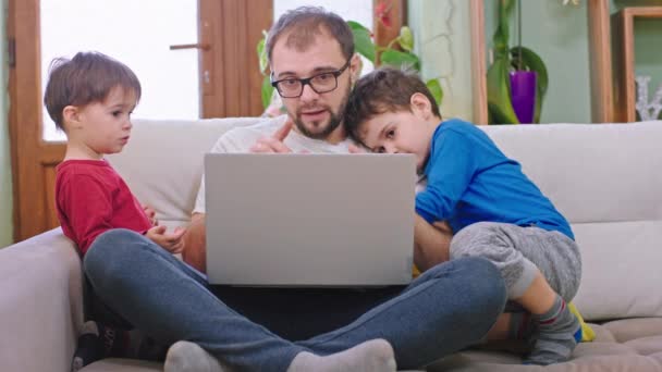 Zbliżenie przed kamerą ojciec z dwójką małych synów przyspiesza piękny czas razem przytulają się i całują siedząc na kanapie. 4k — Wideo stockowe