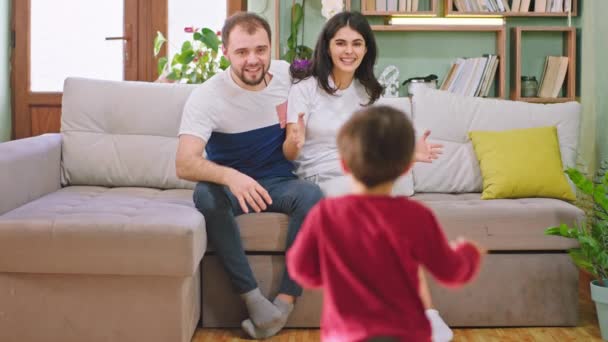 Uśmiechnięci duzi rodzice siedząc na kanapie w salonie, ciesząc się czasem spędzonym z dziećmi, przytulają się do siebie i czują się bardzo szczęśliwi w domu. — Wideo stockowe