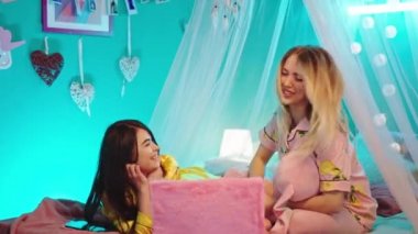 Pijamalı iki genç kadın, dizüstü bilgisayarlarında büyük bir gülümseme ve heyecan hissederek yatakta güzel bir pijama partisi yapıyorlar.