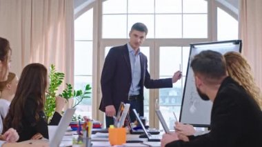 Beyaz adam koçu ofisteki iş adamları için kurumsal bir sunum yapar. Beyaz tahtada yeni bir iş planı sunar ve diğer katılımcılarla tartışır.