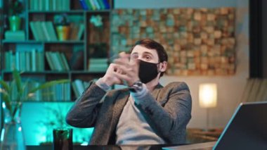 Modern bir ofiste ana yemlik telefonunda koruyucu bir maske takıyor bir ofis çalışanı kalem atıyor kalemi yakalıyor ve Coronavirus 2019 'u aramaya devam ediyor. 4k
