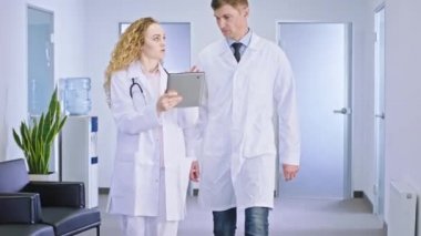 Başhekim ve meslektaşı kadın doktor hastane koridorunda yürüyorlar ve teşhis analizine devam etmek için resepsiyonda durdukları hastanın gelecekteki tedavisini tartışıyorlar.