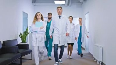 Hastane koridoru kameranın önünde yürüyor. Ana doktor ve büyük hastane ekibi hemşireler ve doktorlar doğrudan kameraya bakıyor.